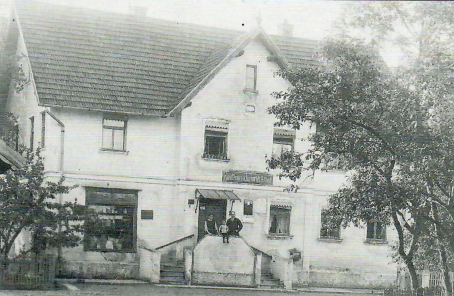 Das „Kaufhaus v. Heinrich Ammann" 1921 (heute Hauptstr. 5) V.re.: Heinrich Ammann mit Sohn Franz (später Ritterkreuzträger) und Ehefrau Anna. Ganz rechts an der Treppe unten der Postbriefkasten."